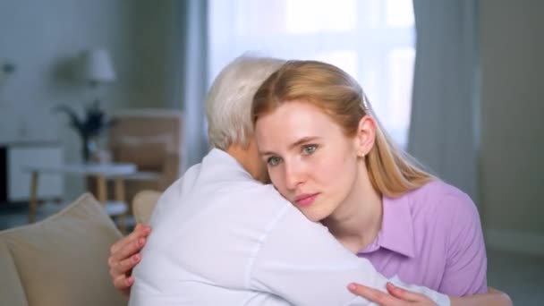 Расстроенная молодая девушка обнимается со своей пожилой матерью на диване — стоковое видео
