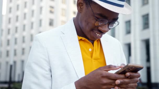 Homem negro alegre em óculos e tipos de terno no smartphone — Vídeo de Stock