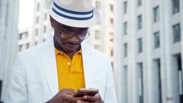 Afroamerikansk man i glasögon och hatttyper på smartphone — Stockvideo