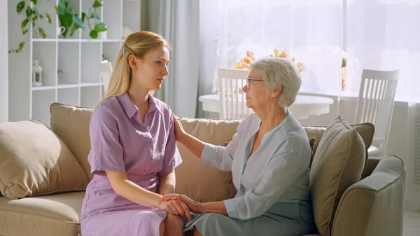 Elderly mother holding hand of young daughter on sofa at home — Stock Photo, Image