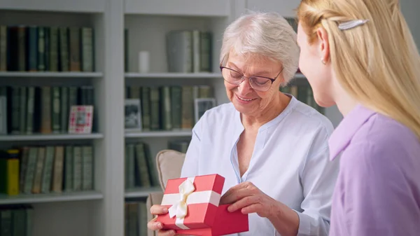 Young daughter giving a gift to an elderly mother for mothers day — Stock Photo, Image