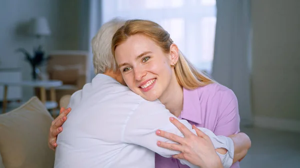 Abbracciare la madre anziana e sorridere figlia nell'appartamento — Foto Stock