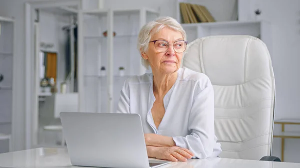 Senior kvinna med kort grått hår sitter på stor vit stol — Stockfoto