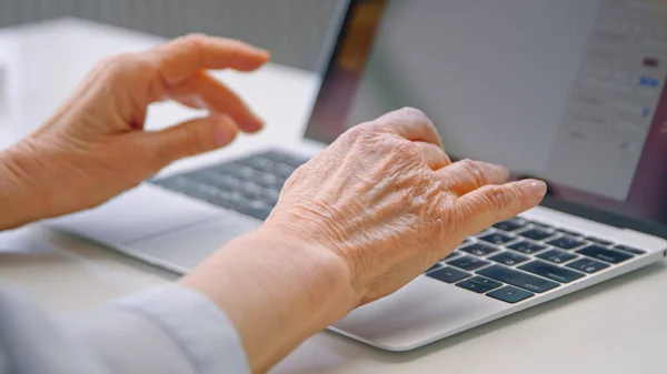 Senior senhora secretária mãos tipo no teclado preto do laptop cinza sentado na mesa branca fazendo trabalho freelance — Fotografia de Stock