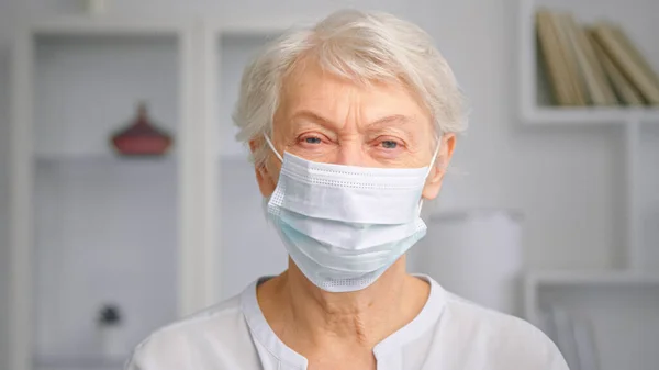 Elderly woman manager with face mask standing against blurred bookshelves — Stock Photo, Image