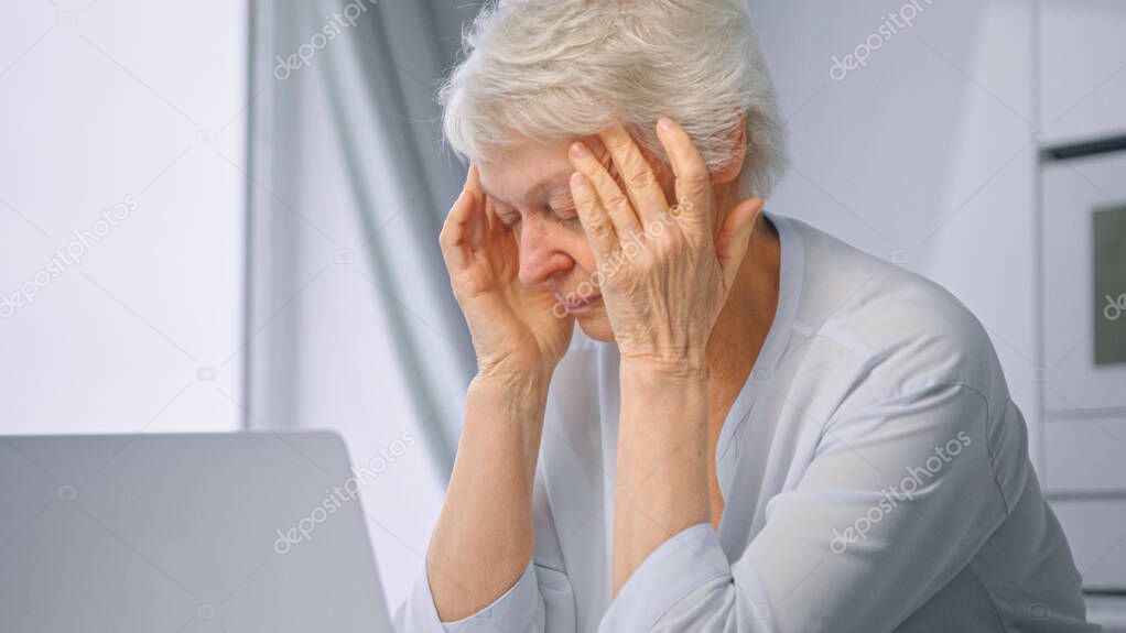 Old tired of work lady pensioner with short grey hair massages temples with hands