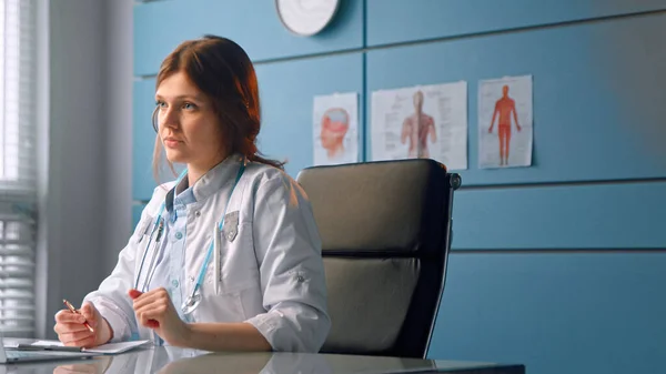 Mujer joven médico habla con paciente mirando hojas de papeles y pantalla gris portátil — Foto de Stock