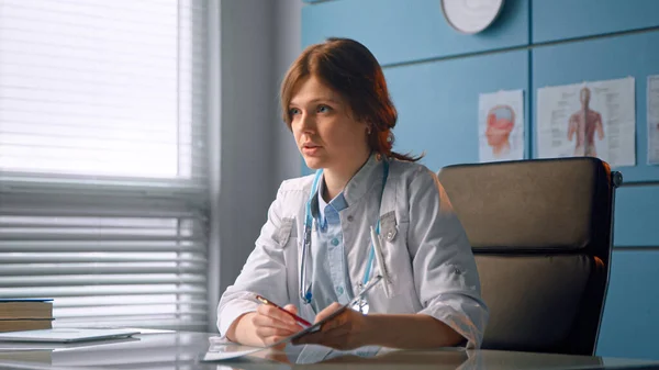Młoda kobieta lekarz wypisuje receptę i rozmawia z pacjentem wyjaśniając diagnostykę na ścianie szpitala — Zdjęcie stockowe