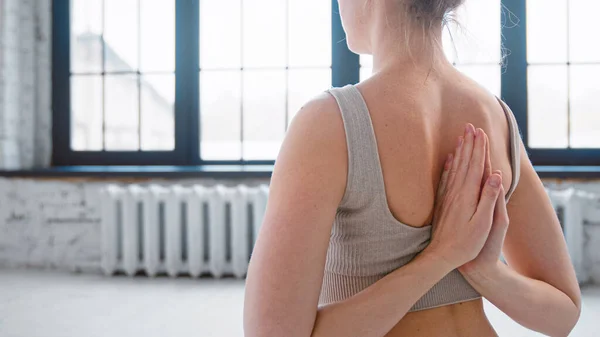 Giovane allenatore di yoga indossa top beige mostra namaste inversa seduta sul pavimento contro la finestra in studio di luce — Foto Stock