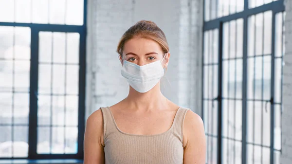 Young lady trainer in tracksuit takes off protective mask looking into camera in spacious studio — Stock Photo, Image