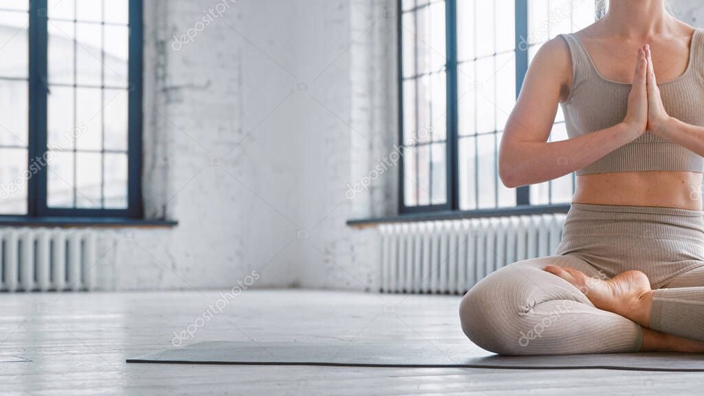 Slim woman in comfortable tracksuit meditates in yoga full lotus position sitting on floor in studio closeup space