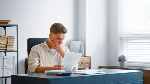 Geschoolde bebaarde accountant in geel shirt kijkt door rapporten op vellen papier — Stockfoto