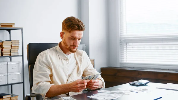 Company director in yellow shirt takes dollar banknotes and puts comparing checks on table in office — Stock Photo, Image