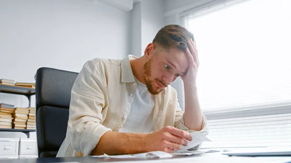 Young man bank accountant with beard looks at paper checks and puts hand on head — Stock Photo, Image