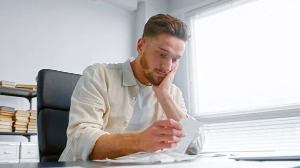 Shocked man bank accountant with beard looks at paper checks and puts hand on head — Stock Photo, Image