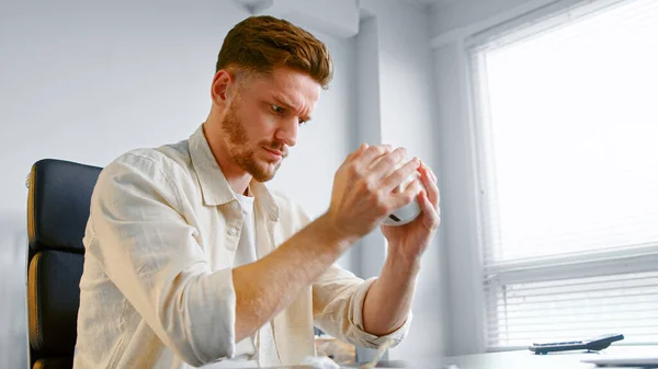 Koncentrerad finansbolagschef håller vit spargris och skakar sittande på grått kontor — Stockfoto