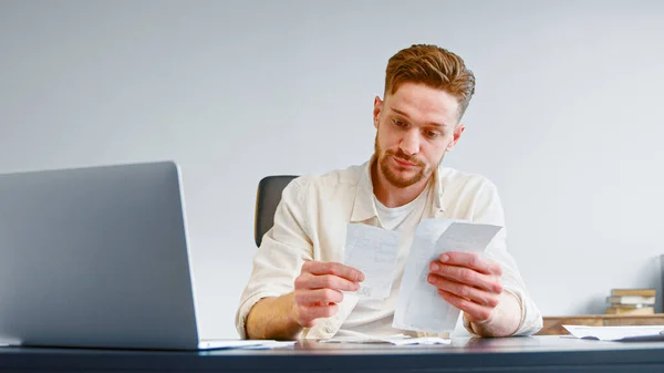 Bearded financial director analyseert papieren cheques op zoek naar geldverspilling en onverwachte uitgaven aan tafel — Stockfoto