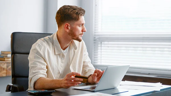 Young man with beard pays online holding credit card Stock Picture