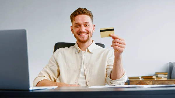 Lächelnder Typ erfolgreicher Firmenmanager mit Bart hält Kreditkarte in der Hand und posiert Stockbild