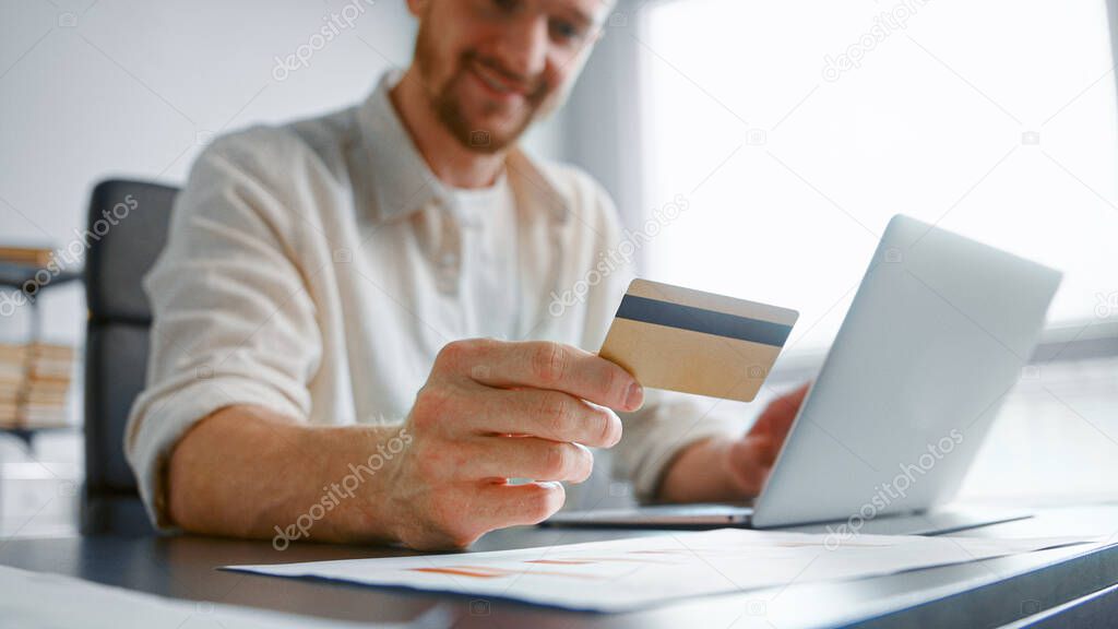 Smiling guy with beard pays company bills online holding yellow card