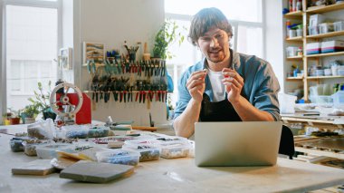 Mutlu adam stüdyoda dizüstü bilgisayar kullanarak eğitim yapıyor. Önlüklü genç bir erkek video ile konuşuyor.