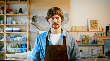 Önlüklü genç adam kameraya bakıyor.