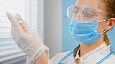 Tek kullanımlık yüz maskesi ve eldiven takan sarışın pratisyen doktor, şırıngayı covid 'e karşı aşıyla dolduruyor.