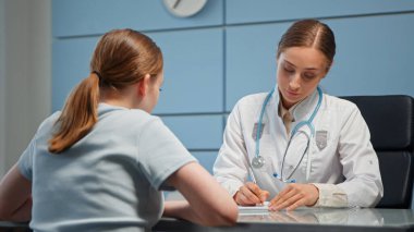 Steteskoplu beyaz önlüklü bayan doktor tıbbi dosyada genç bir kadın için reçete yazıyor.