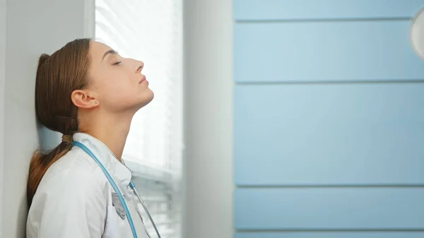 Fiatal nő orvos lélegzik mélyen támaszkodik a falra — Stock Fotó