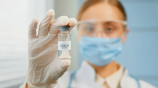 Wazig jonge vrouw medische verpleegkundige in wegwerpmasker en bril houdt coronavirus vaccin vast — Stockfoto