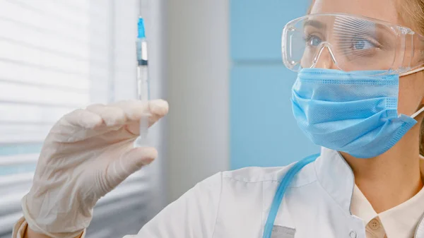 Blond läkare i engångs ansikte mask och handskar fyller sprutan med vaccin — Stockfoto