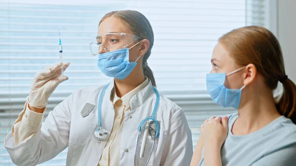 Profesional médico general dama inyecta paciente joven en azul mascarilla desechable —  Fotos de Stock