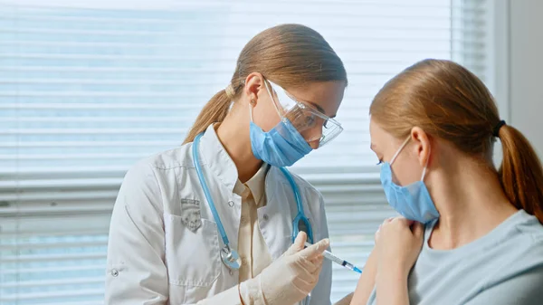 Blond zdravotní sestra v jednorázové obličejové masce a brýle naplňuje injekční stříkačku antivirovou vakcínou — Stock fotografie