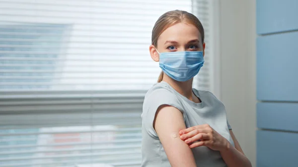 Jonge vrouw blond in blauw wegwerpmasker onderzoekt injectieplek op de onderarm en ziet er recht — Stockfoto