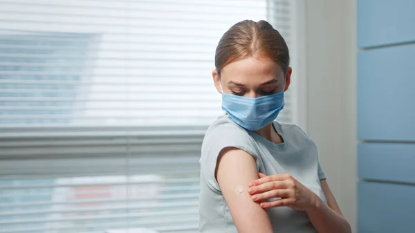 Young girl in blue disposable face mask examines injection spot on forearm — Stock Photo, Image