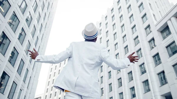 Afro Amerikaanse man in wit pak en Fedora hoed loopt langs grijze stoep dansen en het luisteren naar muziek — Stockfoto