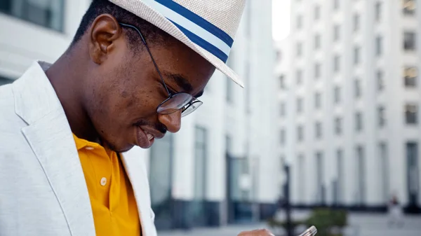 Skoncentrowany Afroamerykanin w okularach i kapeluszu patrzy na wyświetlacz smartfona — Zdjęcie stockowe