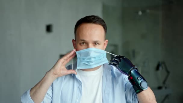 Serieuze kerel met hand prothese kijkt en zet op masker — Stockvideo