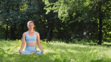 Yoga pozisyonunda çayırda meditasyon yapan konsantre genç bir kadın.