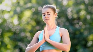 Mavi eşofmanlı kadın yoga uygulayıcısı ayakta meditasyon yapıyor.