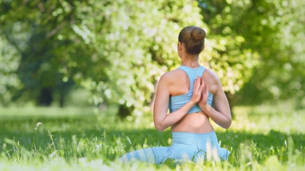 Young woman with hair bun in blue tracksuit practices yoga — Stock Video