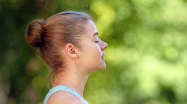 Genç sarışın kadın yoga pozunda yeşil çimlerin üzerinde oturuyor.