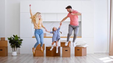 Sevinçli ebeveyn bayan ve erkek anaokulu kızıyla birlikte yeni bir apartman zeminine atlayıp büyük bir karton karton karton karşısında el ele tutuşuyorlar.