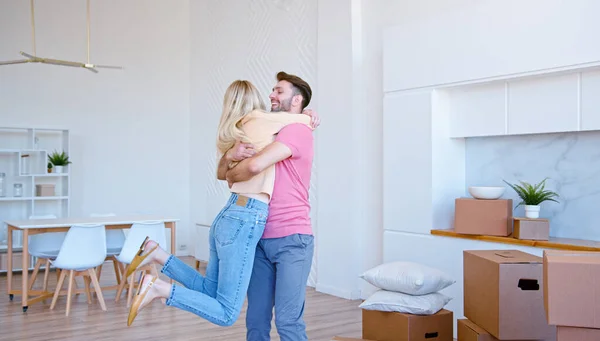 愛の素晴らしいカップルは、新しいアパートの床に大きな段ボール箱を置き、明るい笑顔で回転抱擁 — ストック写真