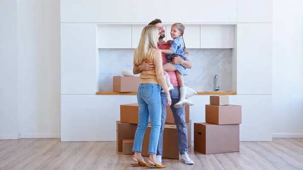 Joyful familie met kind meisje draagt verschillende kartonnen dozen in nieuw appartement en zet op grote stapel — Stockfoto