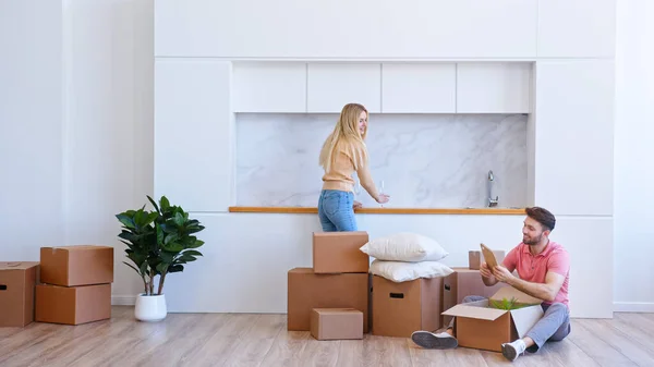 Young woman blonde with long loose hair helps bearded man unpack brown cardboard box in new apartment — Stock Photo, Image