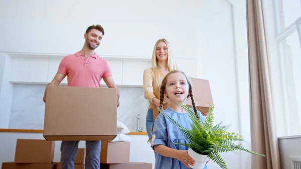 Funny little preschooler daughter looks at parents walking along new apartment with green pot plant — Stock Photo, Image