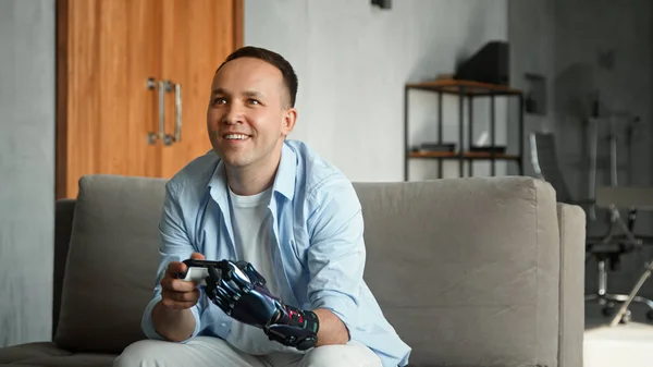Skoncentrowany facet ze sztuczną protezą ręki high tech przegrywa grę konsolową i wyrzuca joysticka — Zdjęcie stockowe