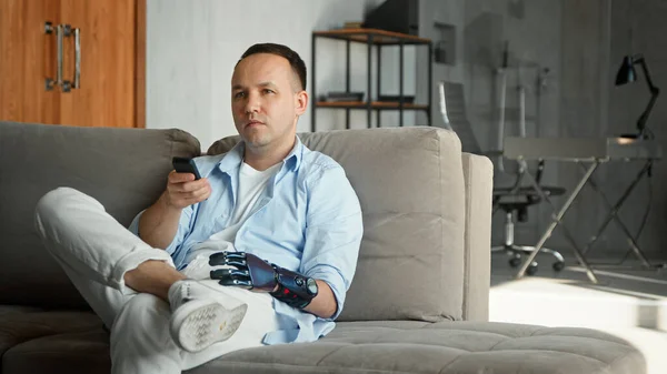 Pria santai dengan teknologi tinggi bio tangan prothesis mengambil remote controller — Stok Foto
