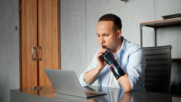 Серьезный программист-киборг с искусственным протезом конечностей смотрит вокруг, сидя за столом